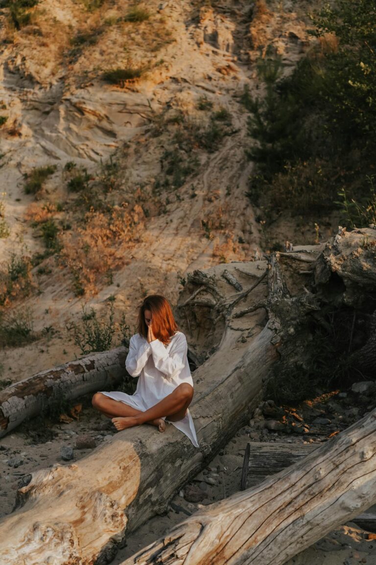 Woman meditating outdoors among logs, embodying peace and mindfulness.