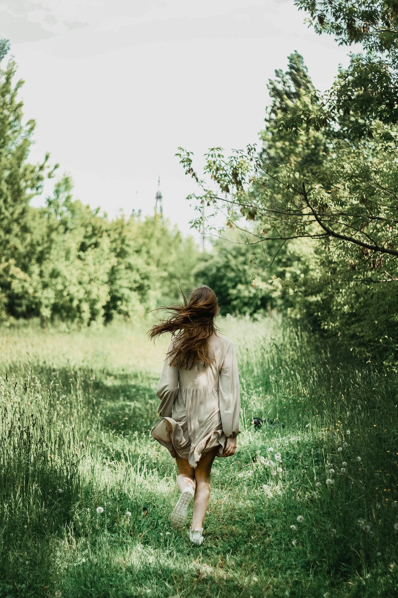 Woman strolling on grassy forest path in sunlight, embracing nature on a bright day.